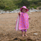 A happy child on a beach, wearing a UV Protective Sun Hat Pink Starfish, pointing towards the camera with a big smile.